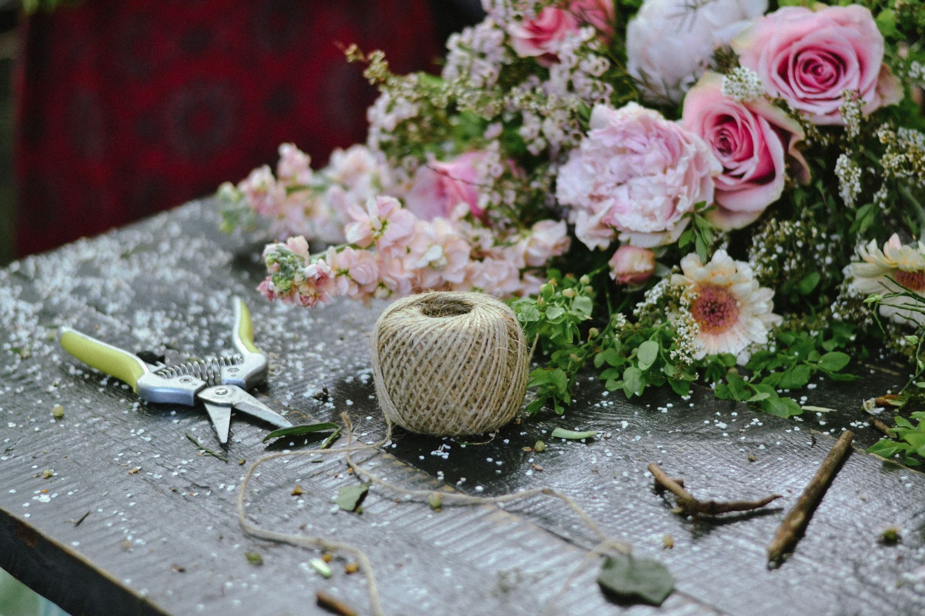 A rustic florist&rsquo;s table with pink roses and peonies, pruning shears, and a spool of twine