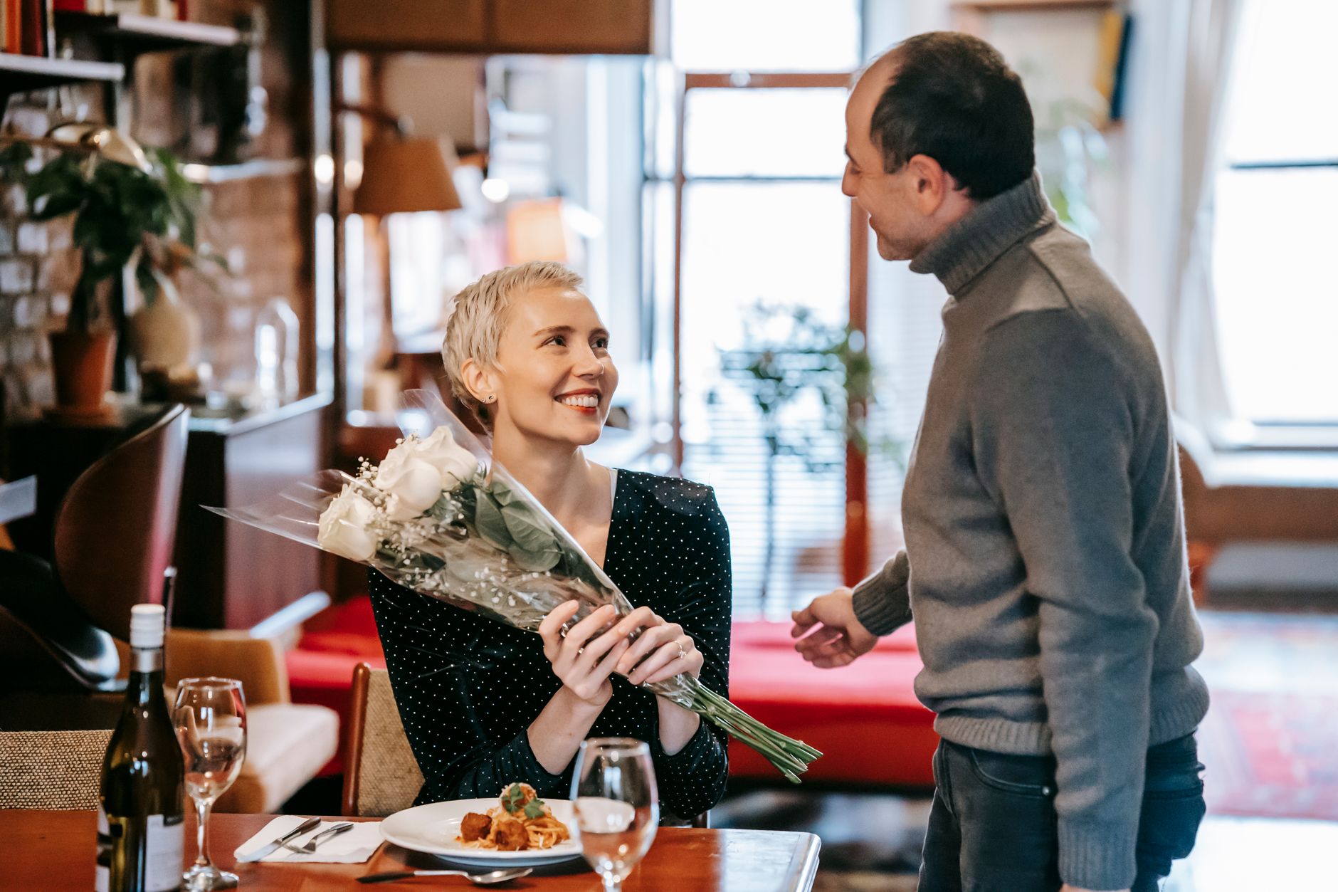 A man gives a smiling woman a bouquet of white roses at a restaurant table