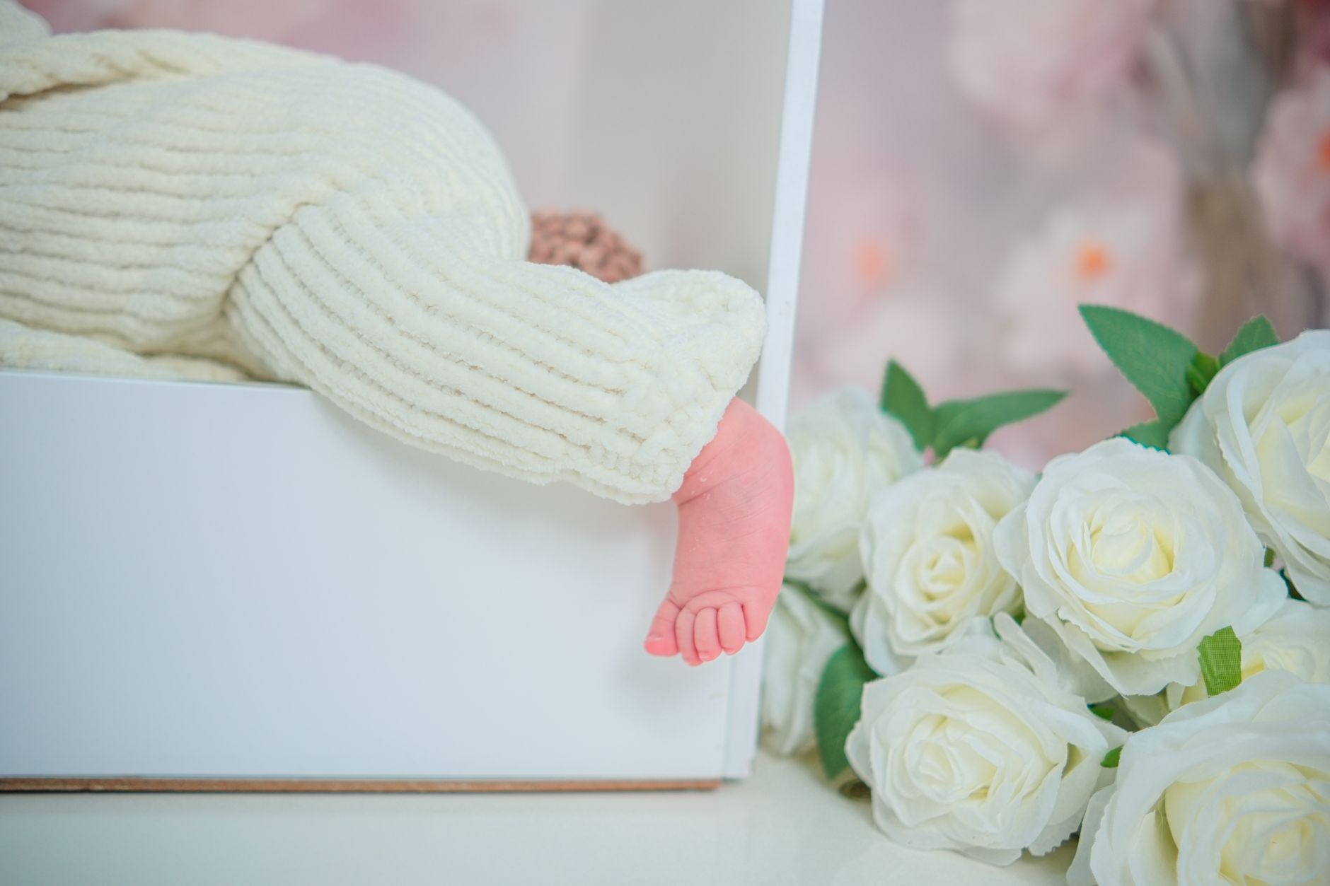 A newborn&rsquo;s foot resting in a white box beside a cluster of cream roses