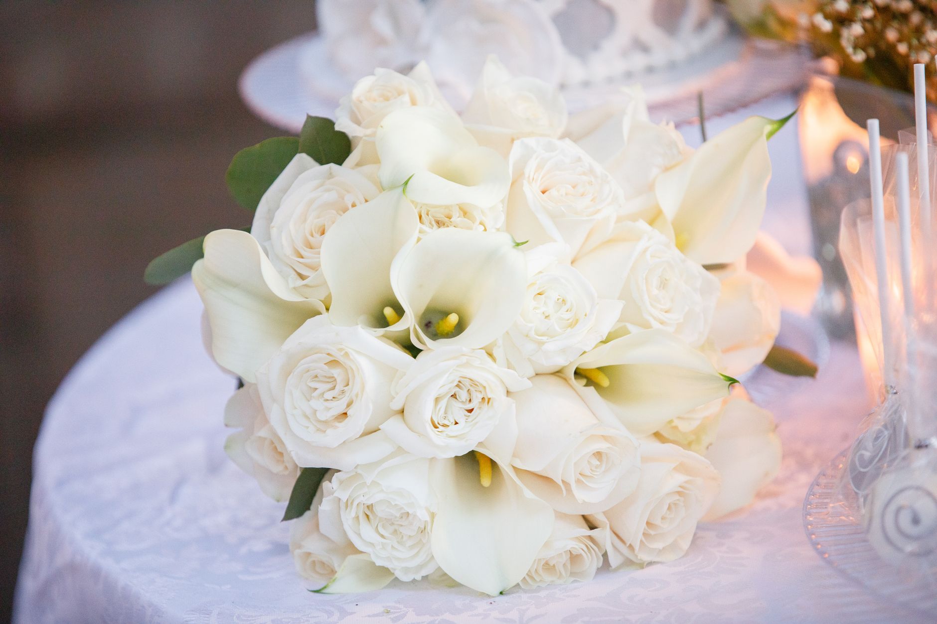 A bridal bouquet of white roses and calla lilies on a draped reception table