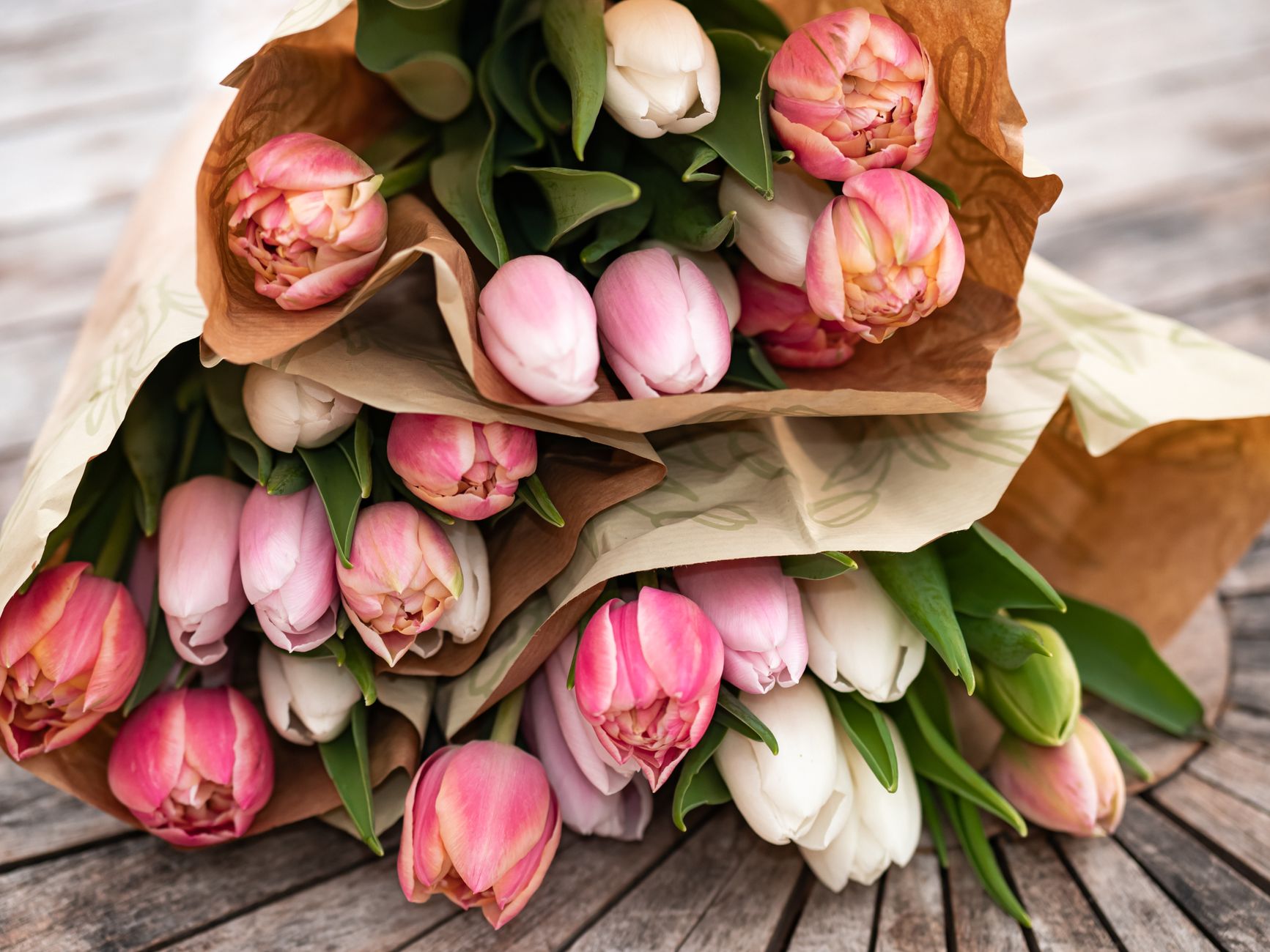 A bouquet of pink and white tulips wrapped in kraft paper on a wooden table
