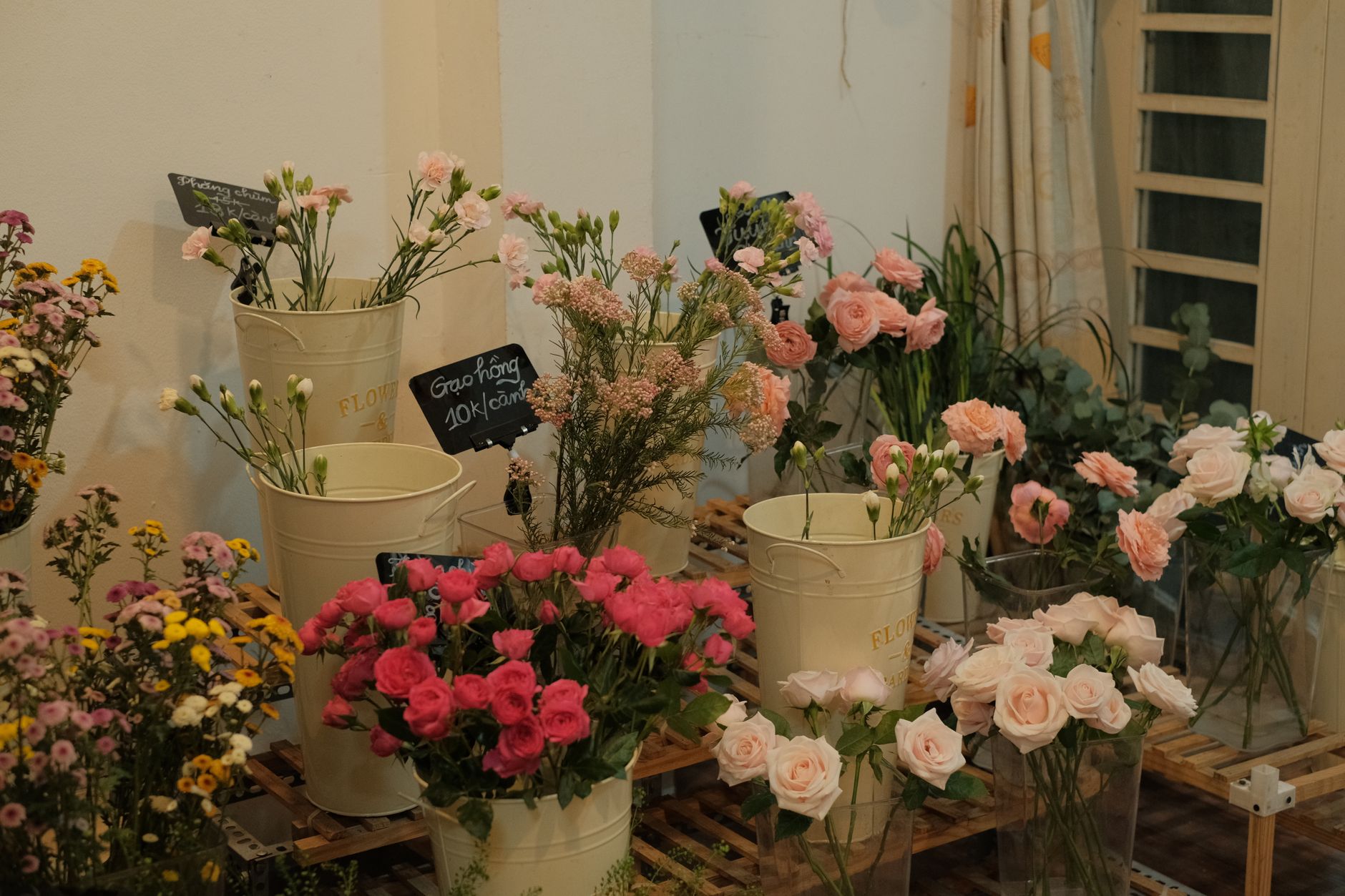 A florist display of pink roses, lisianthus, and mixed blooms in white buckets inside a shop