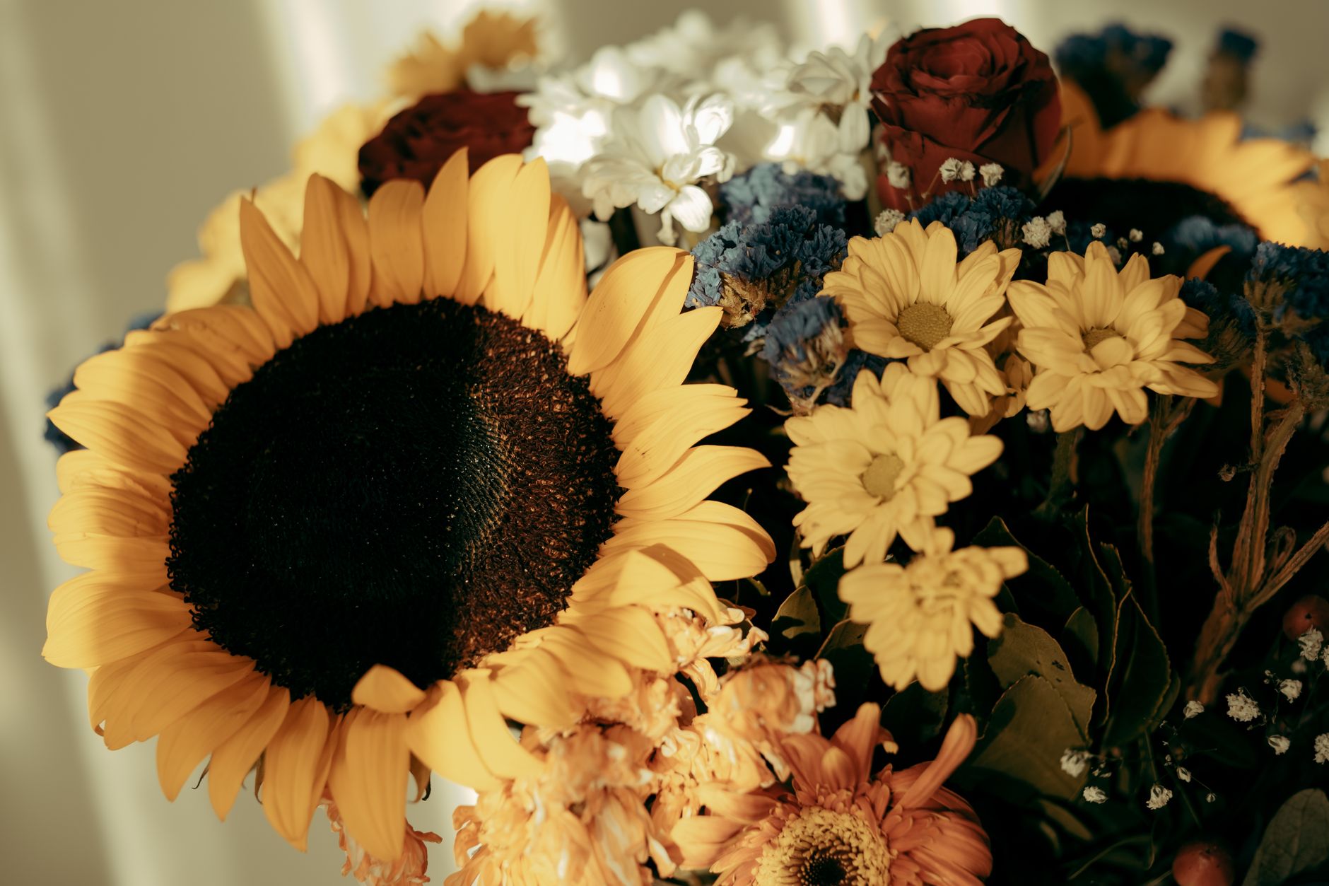A summer bouquet with a large sunflower, blue thistle, daisies, and deep red roses