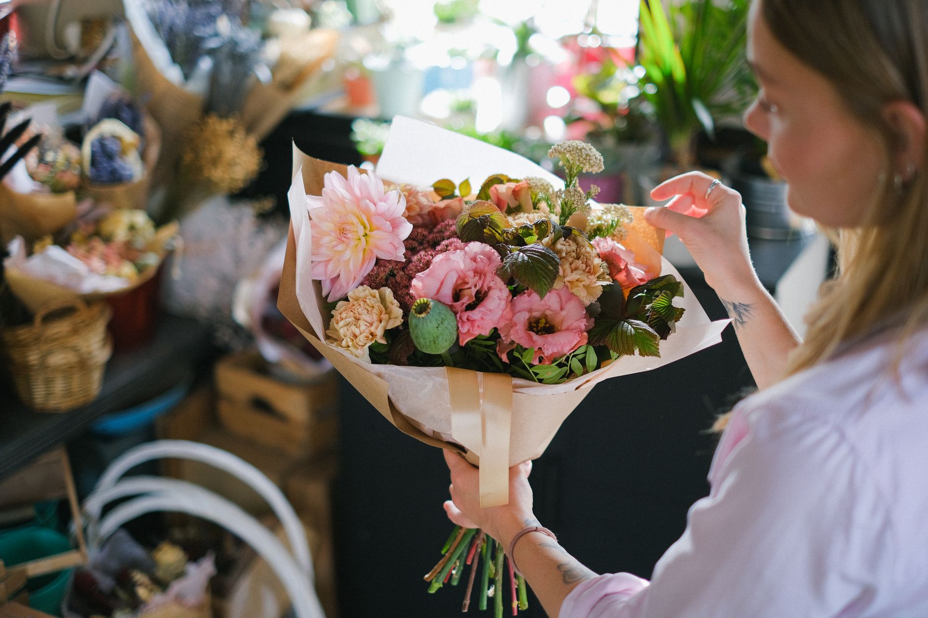 A woman holding a freshly wrapped bouquet of pink roses and soft blooms in a flower shop