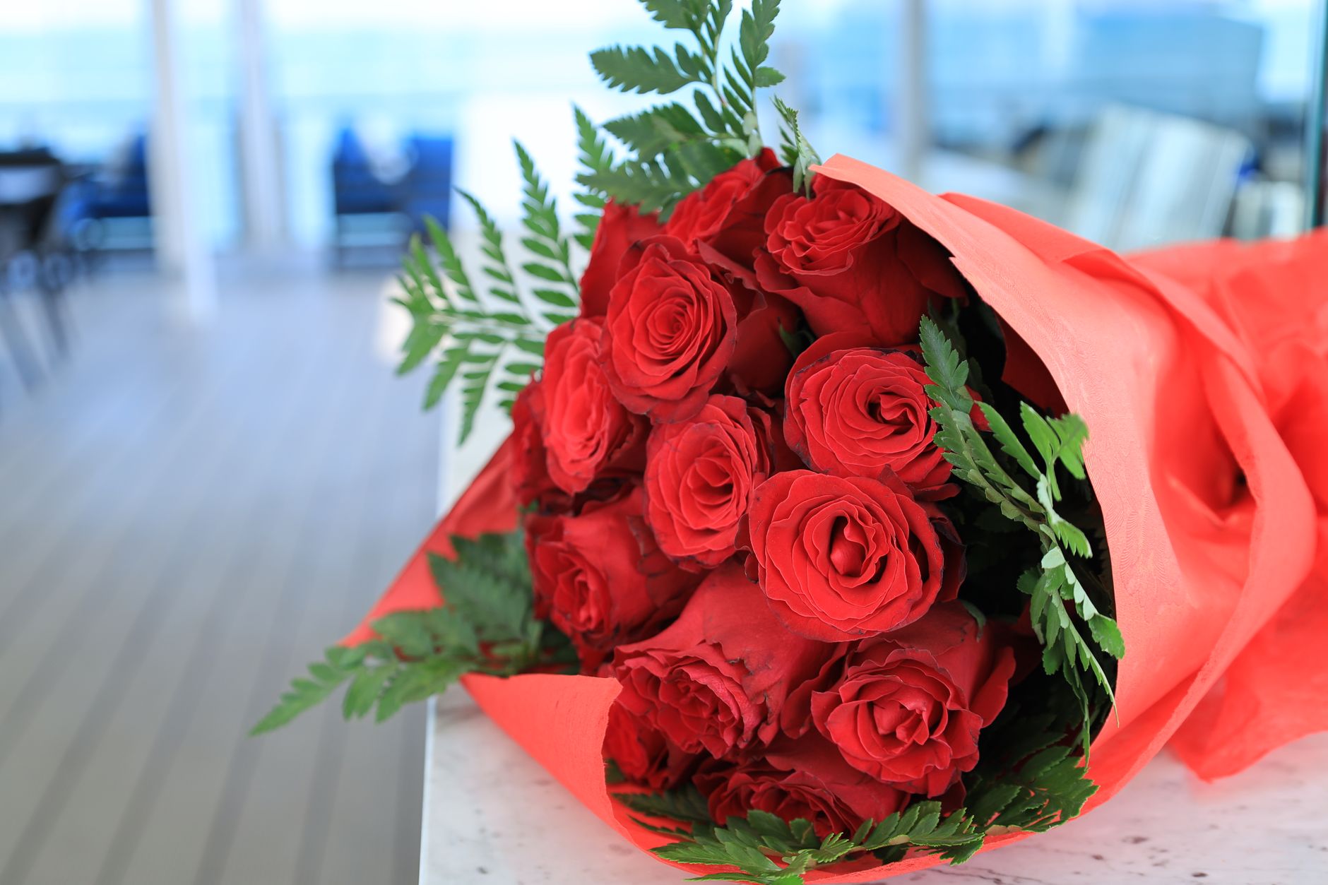 A hand-tied bouquet of a dozen red roses wrapped in paper, resting on a table