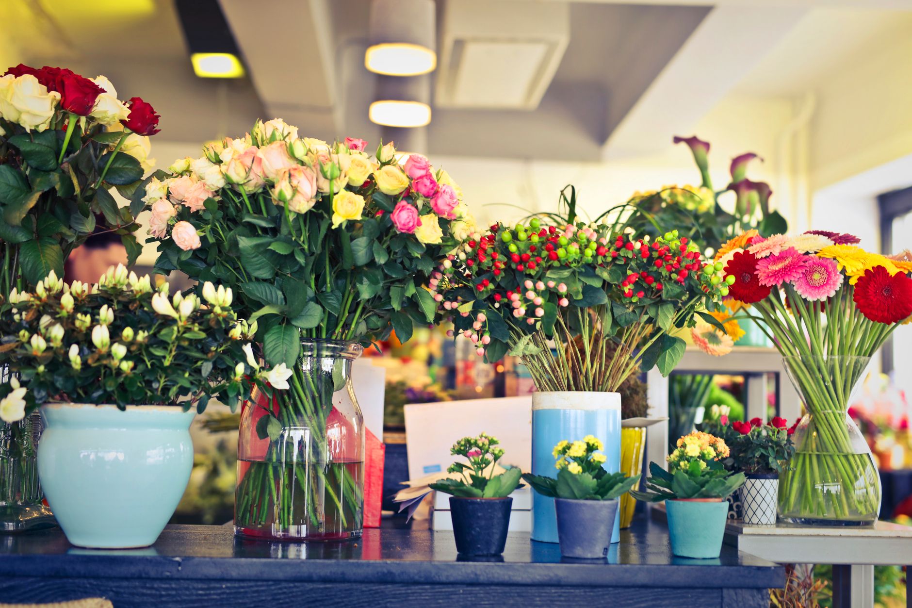 A bright flower shop with vases of roses, lisianthus, and mixed bouquets on a dark counter