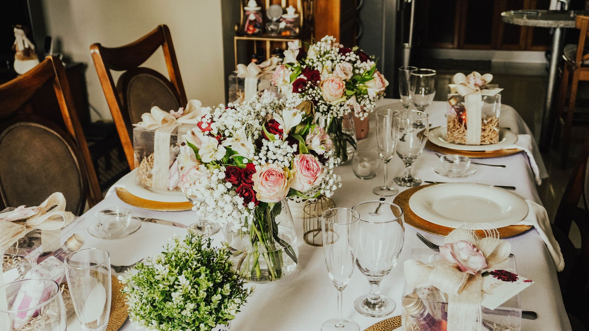 A festive table set with bouquets of roses and baby&rsquo;s breath, wrapped favors, and gold charger plates