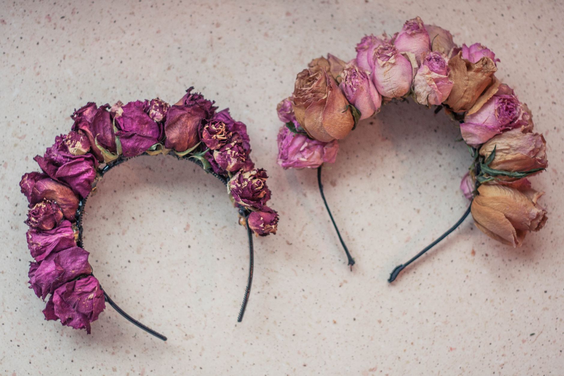Two headbands covered in dried pink and purple roses lying side by side on a pale surface