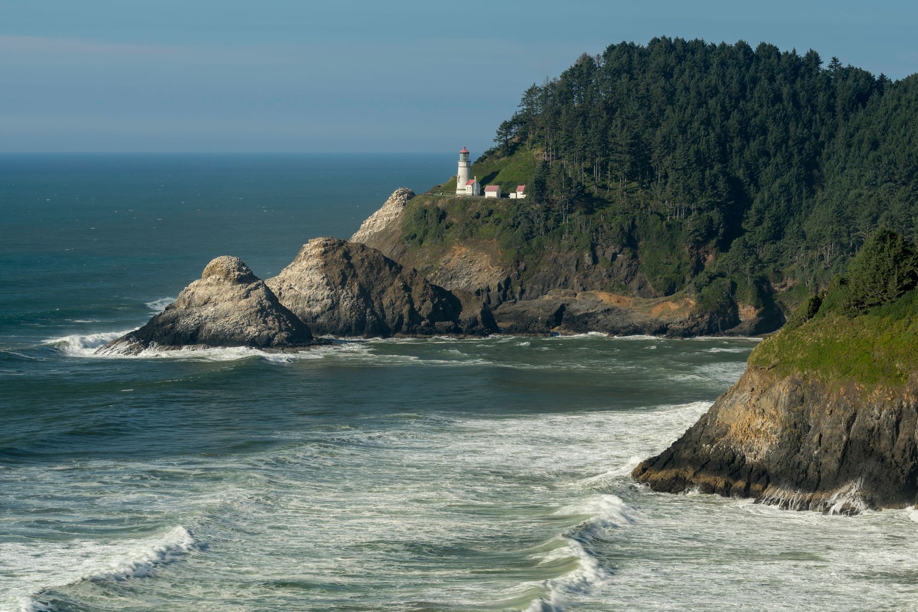 Heceta Head Lighthouse on a forested headland above waves and rocky sea stacks on the central Oregon coast