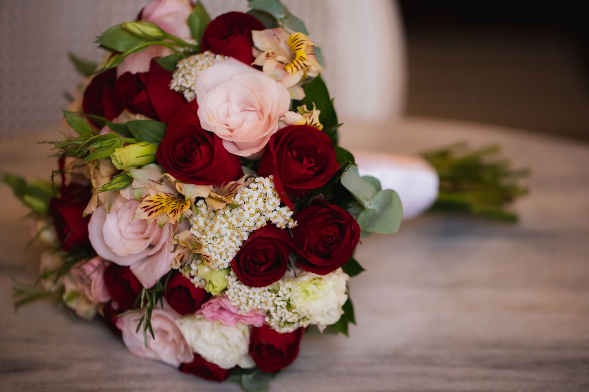 A rounded bouquet of red roses, pink roses, white lisianthus, and alstroemeria on a wooden table