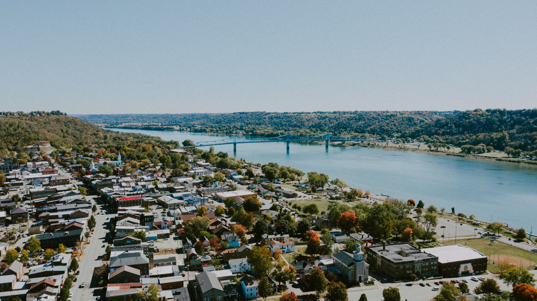 An aerial view of a small river town with a bridge, brick buildings, and fall color