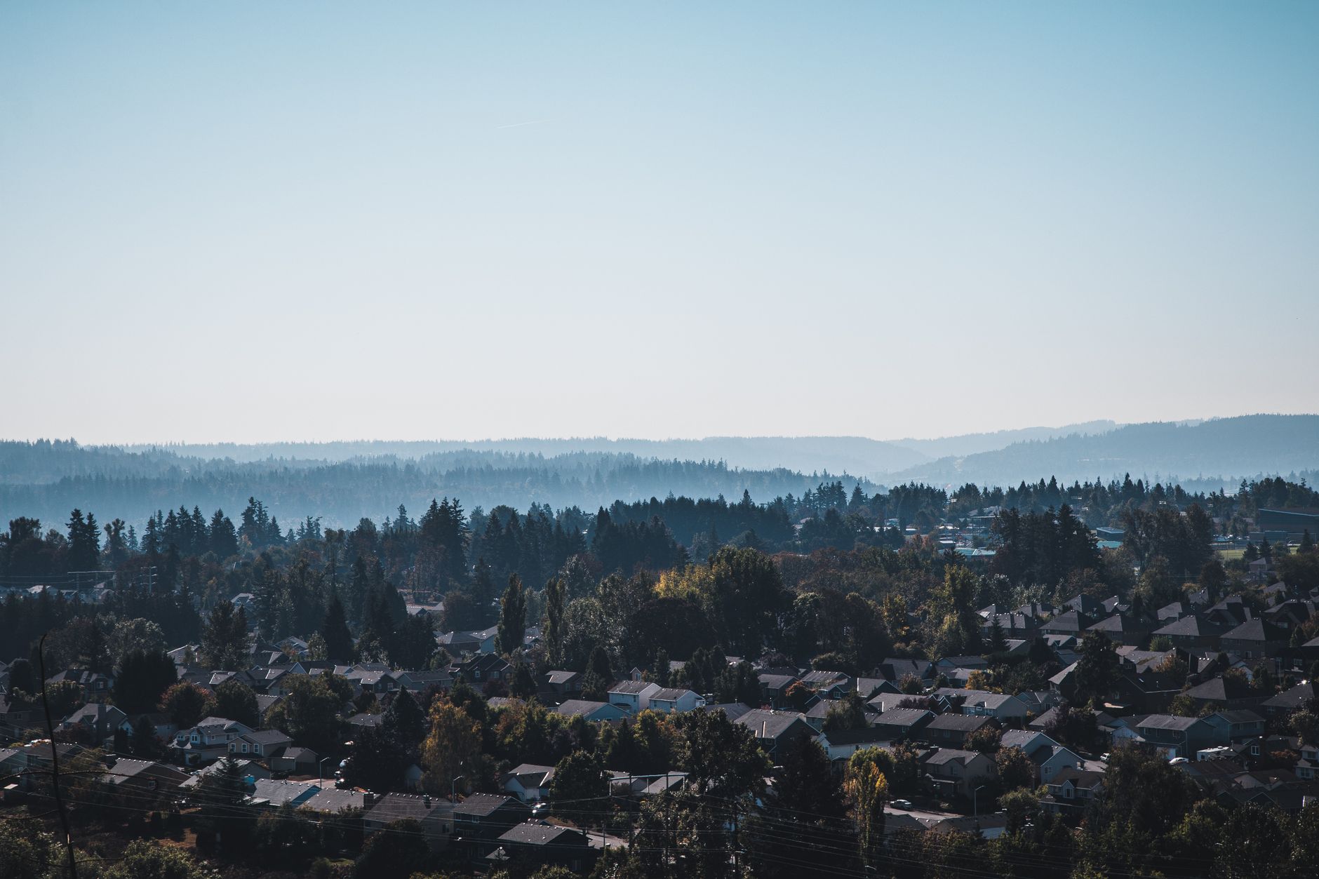 A hazy aerial view of houses and evergreen trees with forested hills in the distance