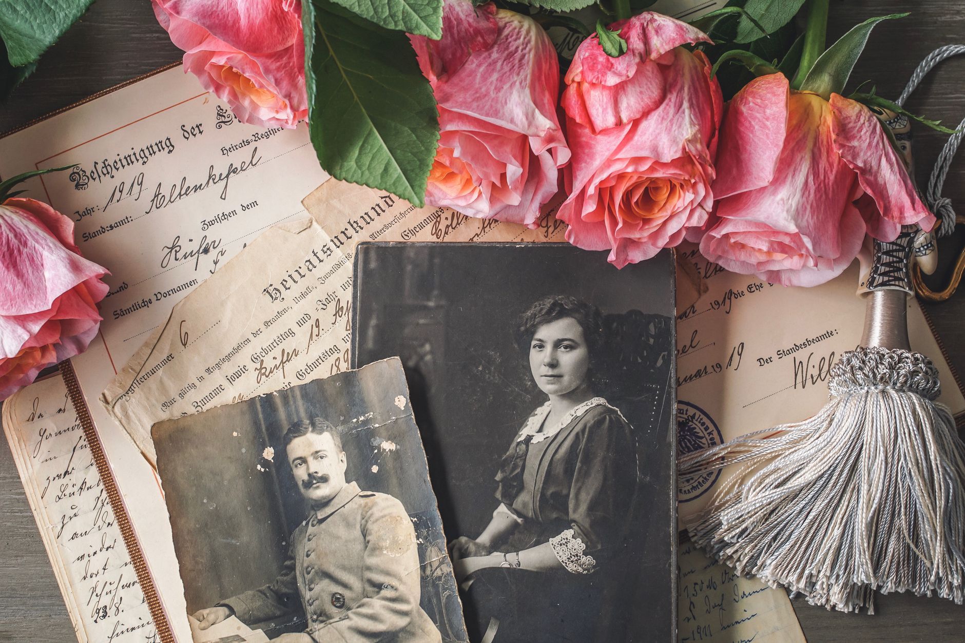 Pink roses resting on old photographs and handwritten documents with a silver tassel