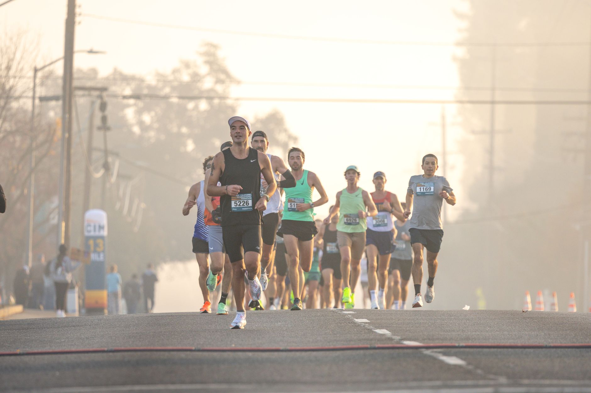 A group of marathon runners on a hazy morning street with sunlight behind them