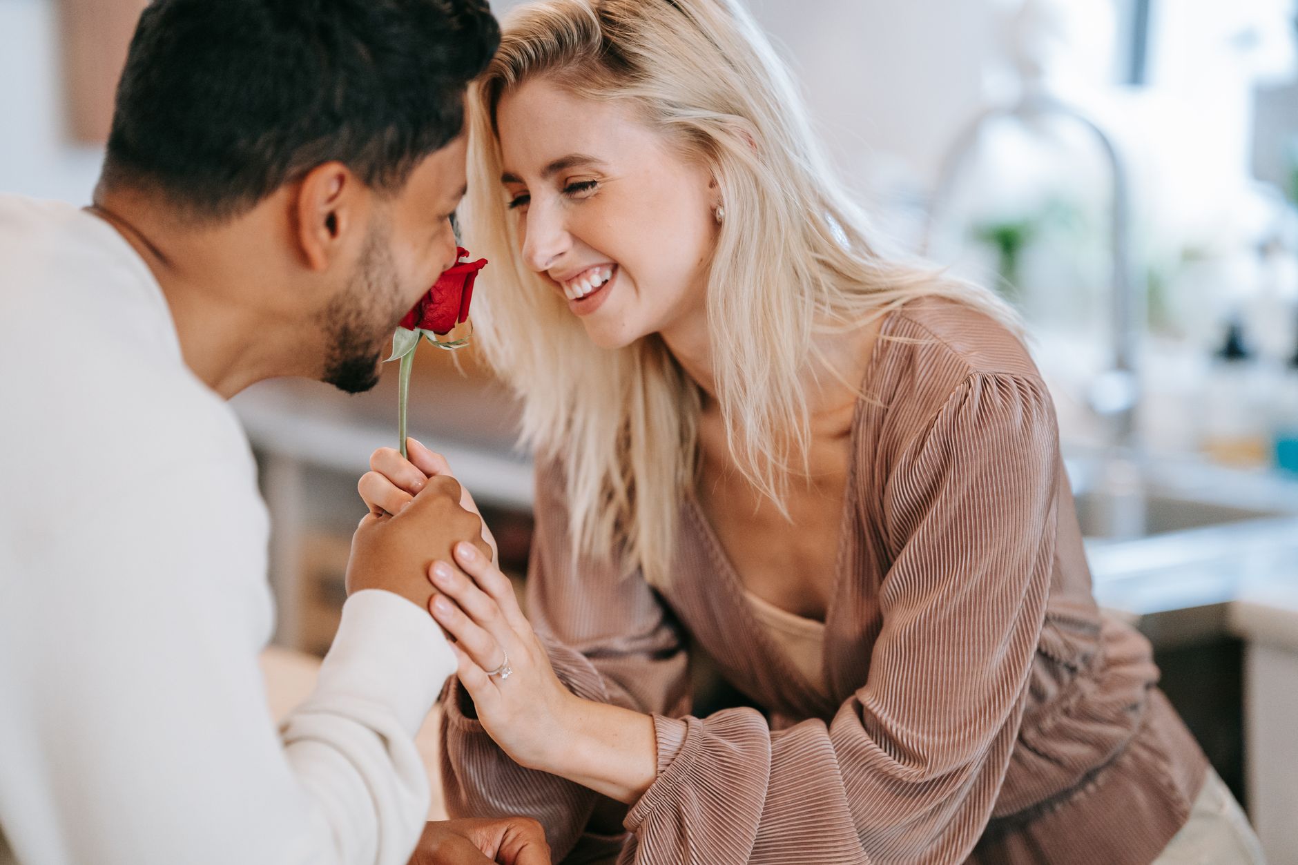 A smiling couple sharing a moment with a single red rose in a bright kitchen