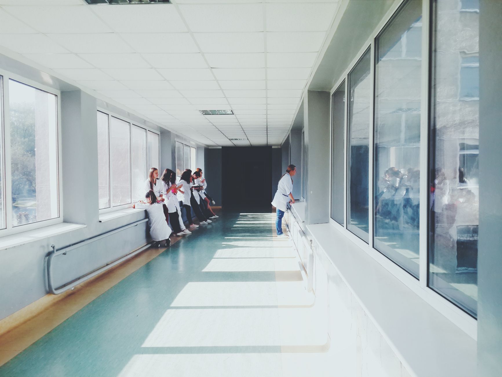 Healthcare workers in white coats gathered at the end of a bright hospital hallway