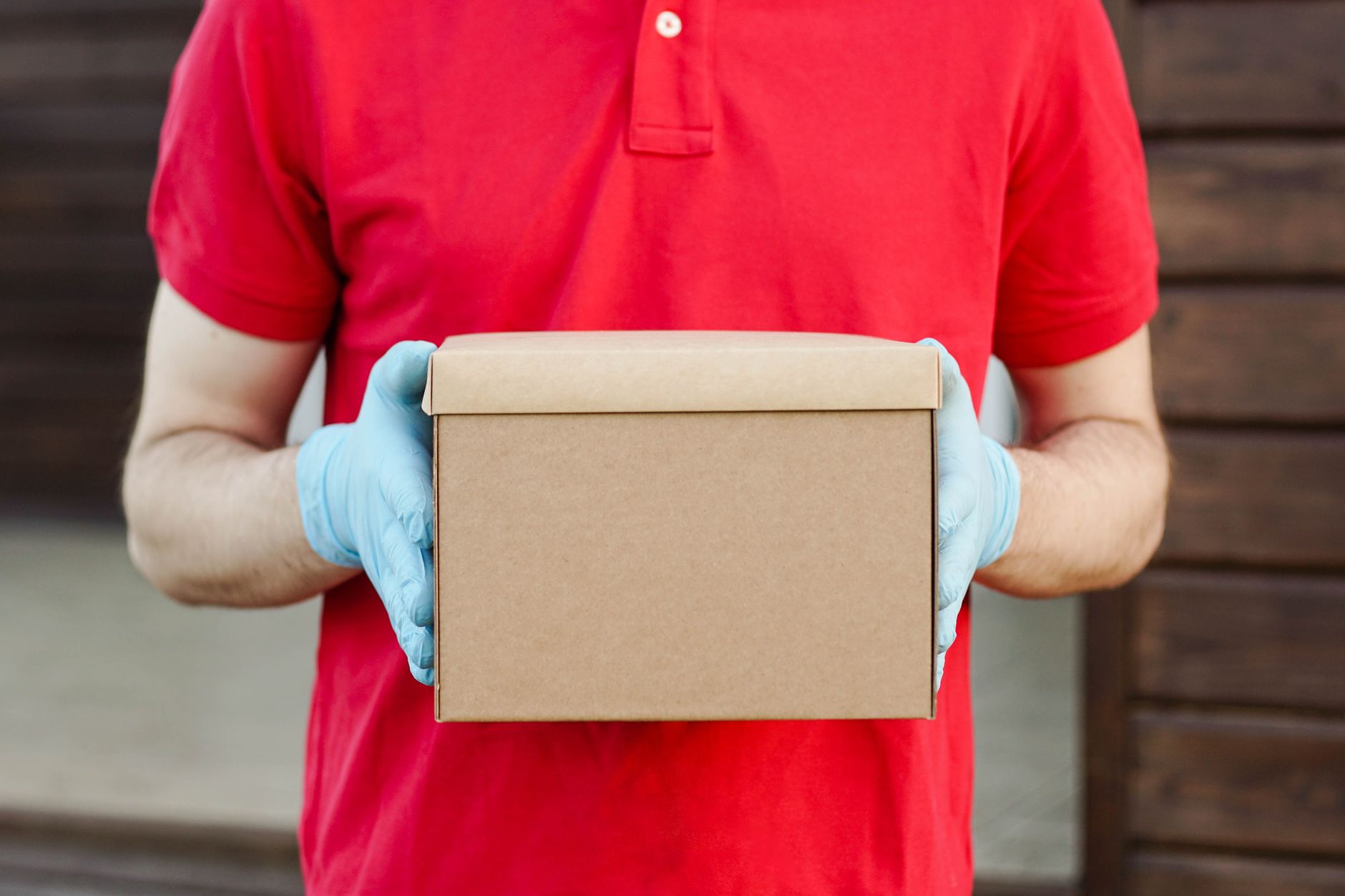 A delivery person in a red polo and blue gloves holding a cardboard package