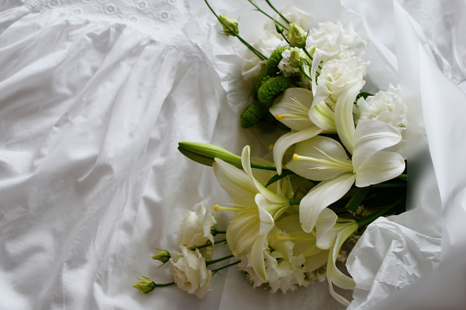 A bouquet of white lilies and carnations resting on white linen
