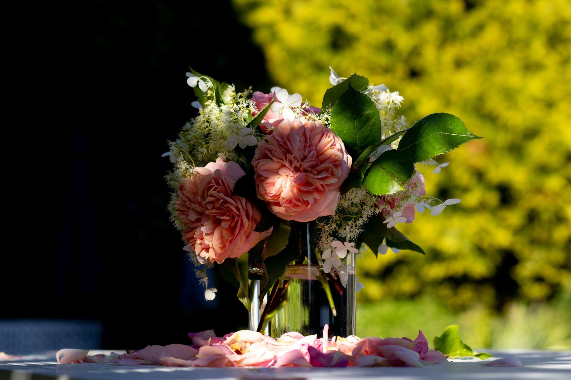 A small bouquet of peach garden roses and white hydrangea in a glass jar on an outdoor table