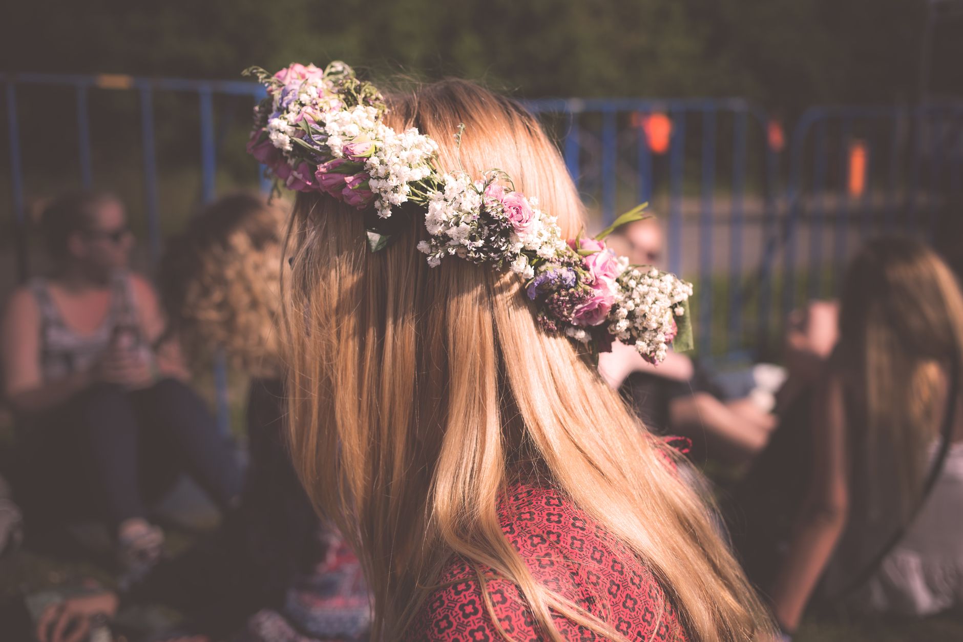 A woman seen from behind wearing a flower crown of white and pink blooms at an outdoor festival