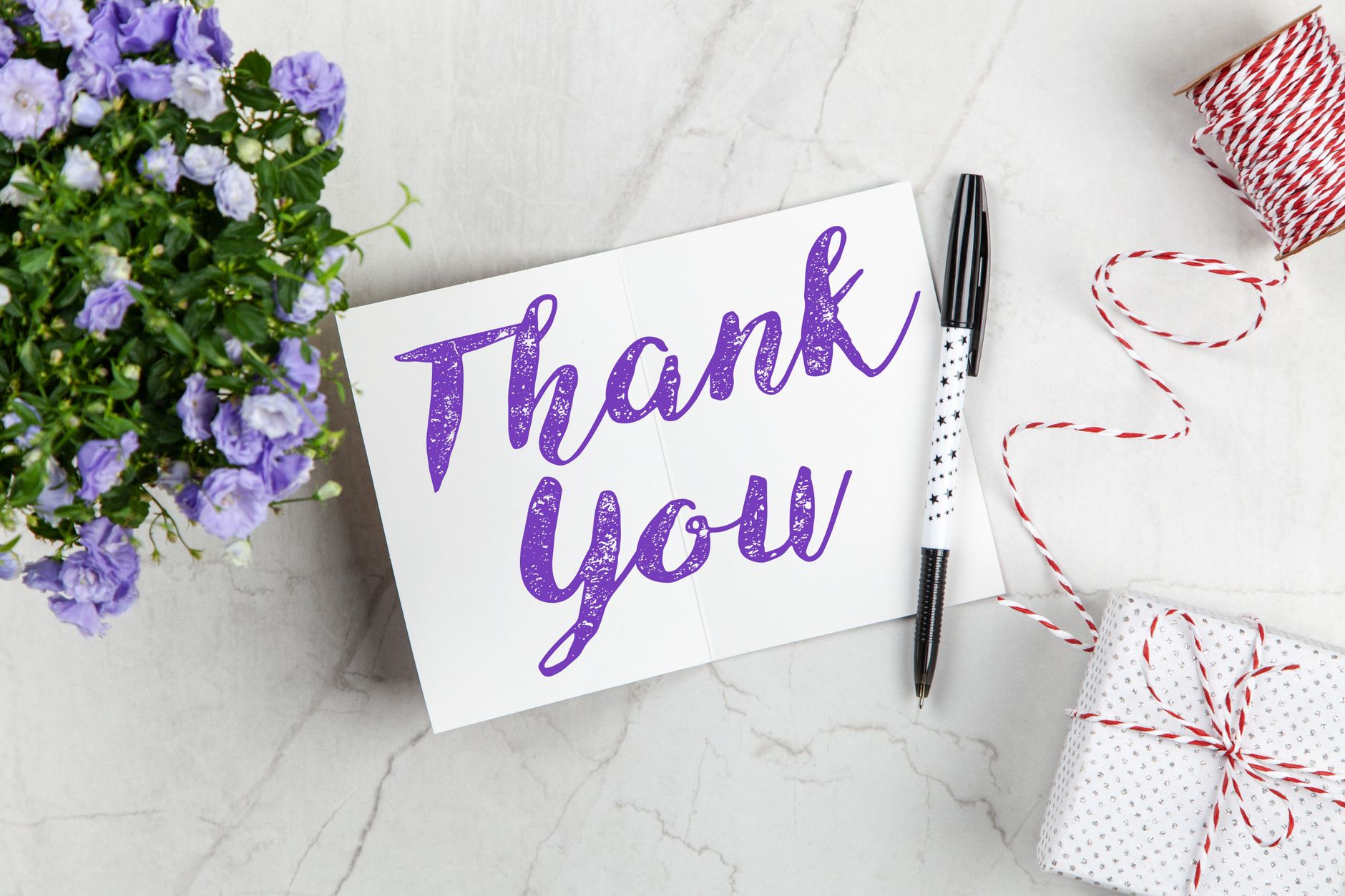 A purple flower bouquet next to a handwritten Thank You card and a wrapped gift